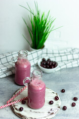 A bottle of cherry smoothies on a white background, cherries in bulk and in a plate. Morning summer breakfast