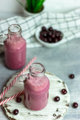 A bottle of cherry smoothies on a white background, cherries in bulk and in a plate. Morning summer breakfast