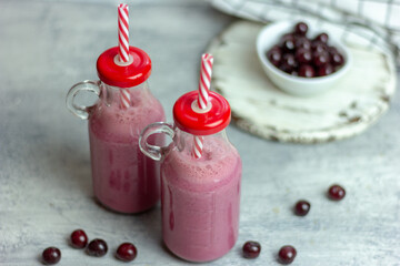 A bottle of cherry smoothies on a white background, cherries in bulk and in a plate. Morning summer breakfast