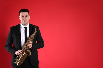 Fototapeta premium Young man in elegant suit with saxophone on red background. Space for text