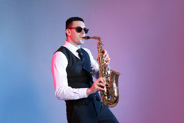 Obraz na płótnie Canvas Young man in elegant outfit playing saxophone on color background