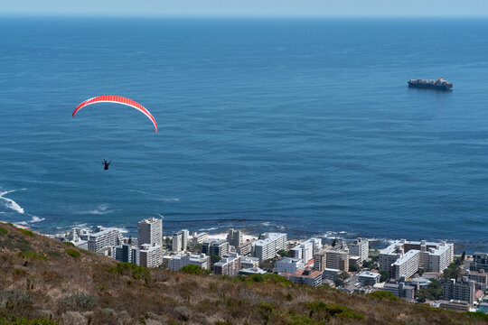 Red paraglider over city with blue sea and ship.