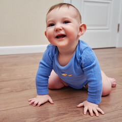 Happy baby toddler crawls on a wooden laminate. Funny child is sitting smiling on the parquet in the home living room, aged 6-11 months