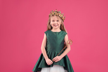 Cute girl in fairy dress and golden crown holding magic wand on pink background. Little princess