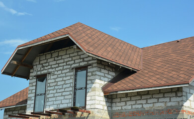 Fototapeta premium A close-up of an attic of one and a half storey house under construction with dormer windows, asphalt shingled roof, and the beginning of a loft balcony construction.Asphalt shingles roofing.