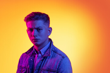 Closeup young handsome man wearing casual youth style clothes isolated on orange background in neon light, filter. Concept of emotions, beauty, fashion