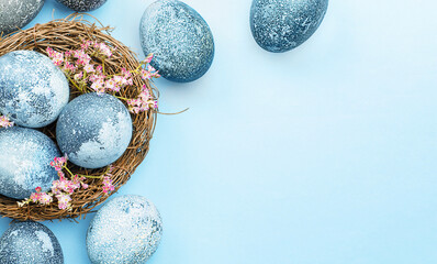 blue easter eggs and spring flowers in a nest on a blue background