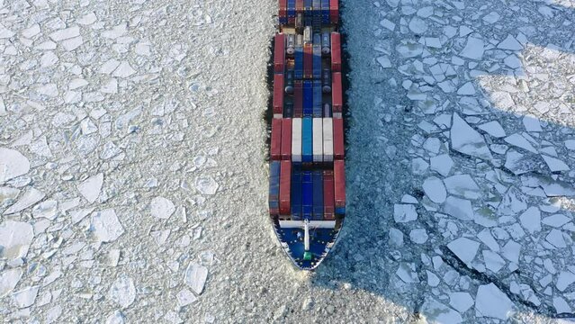 St. Petersburg, Russia, winter 2022: Cargo container ship running through the ice floe, top aerial view of bow. Sunny winter day, ice floes around the ship