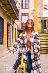 Pretty latin woman with sunglasses doing bicycle sightseeing in the city through the old town. Eco-tourism lifestyle in spring