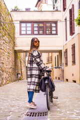 Obraz premium Pretty latin woman with sunglasses doing bicycle sightseeing in the city through the old town. Eco tourism in spring on vacation