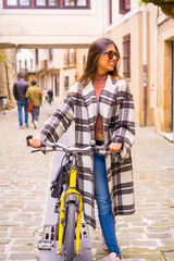 Fototapeta na wymiar Pretty latin woman with sunglasses doing bicycle sightseeing in the city through the old town. Ecological tourism in spring on vacation, looking to the right
