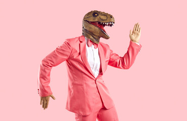 Lustiger Mann in Gummidinosauriermaske tanzt und hat Spaß im Studio. Fröhlicher Typ mit Echsenkopf in stylischem, funky, leuchtend rosa Partyanzug, der ägyptische Tanzbewegungen einzeln auf rosafarbenem Hintergrund macht