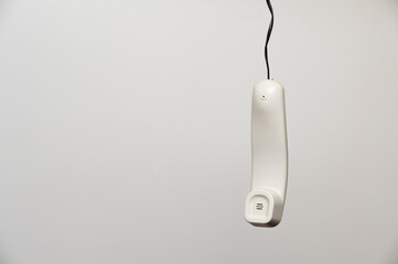 A hanging white handset of an outdated home phone