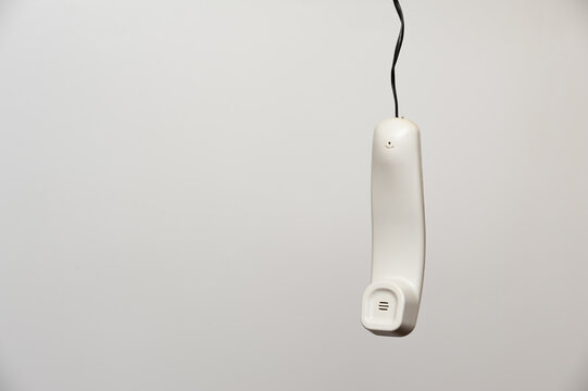 A hanging white handset of an outdated home phone