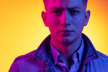 Closeup young handsome man wearing casual youth style clothes isolated on orange background in neon light, filter. Concept of emotions, beauty, fashion