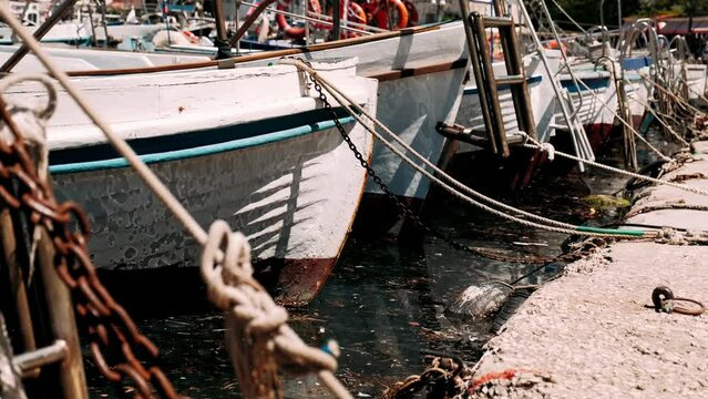 Old wooden fishing boats on dark water of sea moored to pier with ropes in small port of ancient seaside town close view.