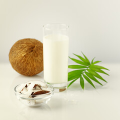 Natural non diary coconut milk. Vegan food composition with glass of coconut milk, coconut and palm leaves on a white table. Still life with vegan healthy product
