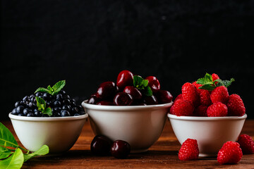 a variety of wild berries in a bowl on a wooden background. rasp