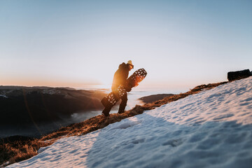 Snowboarder in sportswear hiking in the mountains with snowboard