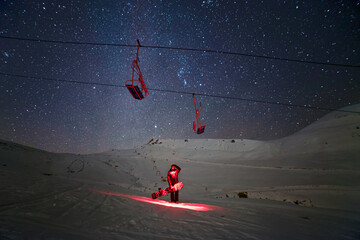 Snowboarder at night under the chairlift with sky full of stars