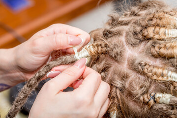 Dreadlocks African braids are weaved by a master hairdresser in the salon, head and hair close-up braided into dreadlocks copy space, boy european