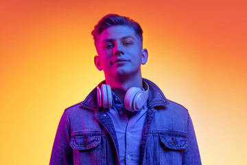 Half-length portrait of young handsome man in casual youth style clothes isolated on orange background in neon light, filter. Concept of emotions, beauty, fashion