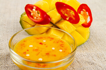 Close-up of diced half of mango, sliced red hot pepper and mango chili sauce on burlap. Rustic...
