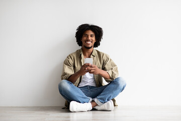 Mobile App. Young black man with smartphone in hands relaxing on floor