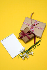 on a yellow background a bouquet of white snowdrops, two gift boxes, a notepad. card, congratulations on March 8