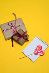 on a yellow background, a red heart-shaped lollipop, two gift boxes, a notepad. card, congratulations on Valentine's Day. romantic background