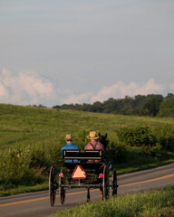 Fototapeta na wymiar Two Amish Men Riding a Horse and Buggy on a County Road with a Hay Field in the Background