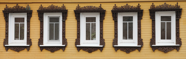 The old window of a rustic Russian wooden house is richly decorated with carvings in an old Russian city.
