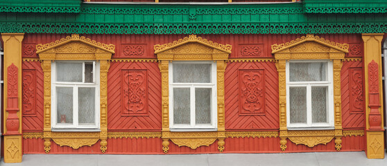 The old window of a rustic Russian wooden house is richly decorated with carvings in an old Russian city.