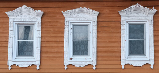 The old window of a rustic Russian wooden house is richly decorated with carvings in an old Russian city.