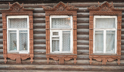 The old window of a rustic Russian wooden house is richly decorated with carvings in an old Russian city.