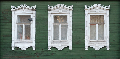 The old window of a rustic Russian wooden house is richly decorated with carvings in an old Russian city.