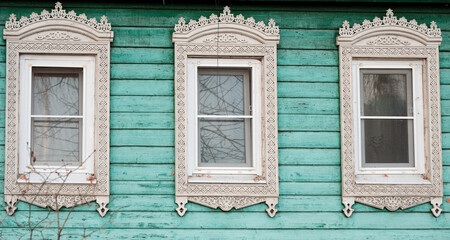 The old window of a rustic Russian wooden house is richly decorated with carvings in an old Russian city.