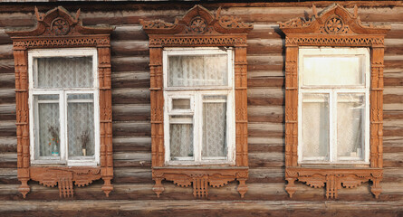 Fototapeta na wymiar The old window of a rustic Russian wooden house is richly decorated with carvings in an old Russian city.