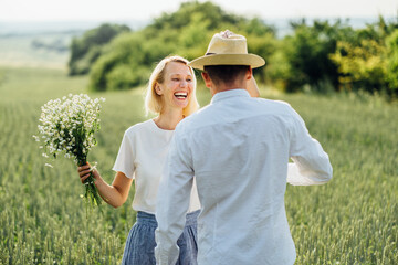 Summer Lifestyle. Summer Lifestyle concept. Young couple resting in field with wild flowers in a wheat field running dancing on summer day.