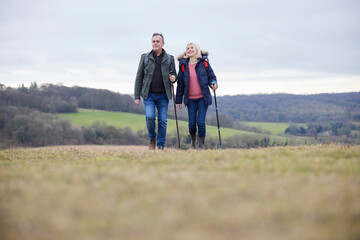 Mature Couple Walk Through Fall Or Winter Countryside Using Hiking Poles
