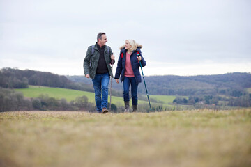 Mature Couple Walk Through Fall Or Winter Countryside Using Hiking Poles