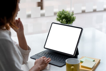 Businesswoman sitting at work using a tablet in front of a white screen.