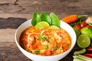 Tom Yum Goong or Shrimp soup spicy sour Soup Traditional food in Thailand contains chili, lime,lemongrass, lime leaf, along with cooked rice in a white dish on the old wood background.