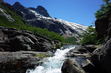 Mountain river in Patagonia, white water bare black rock green bushes snow hills sunny day in Argentina Nahuel Huapi National Park, Nature landscape