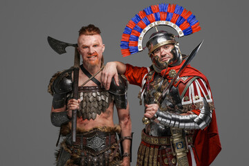Joyful viking and roman soldier posing against gray background
