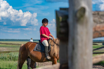 Obraz premium A young beautiful girl in a jockey cap and a red T-shirt rides a horse.