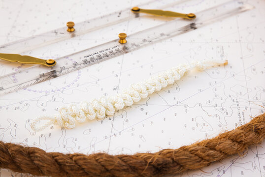 Navigation tools are on the navigation map. A sea ruler, and next to it lies a white rope with knots and a manila rope.