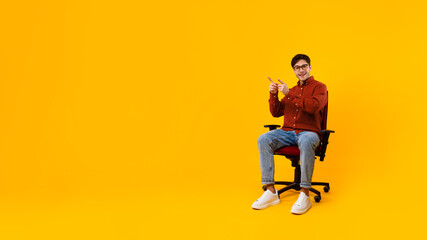 Fototapeta na wymiar Man Pointing Fingers Aside Showing Free Space Sitting, Yellow Background