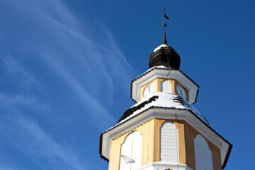 Fototapeta na wymiar A yellow clock tower of an old church with blue sky and white thin cloud on a background