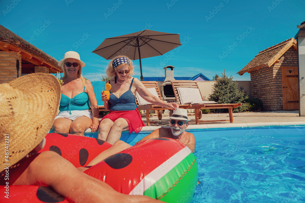 Wall mural two senior couples relaxing at the swimming pool while on summer vacation